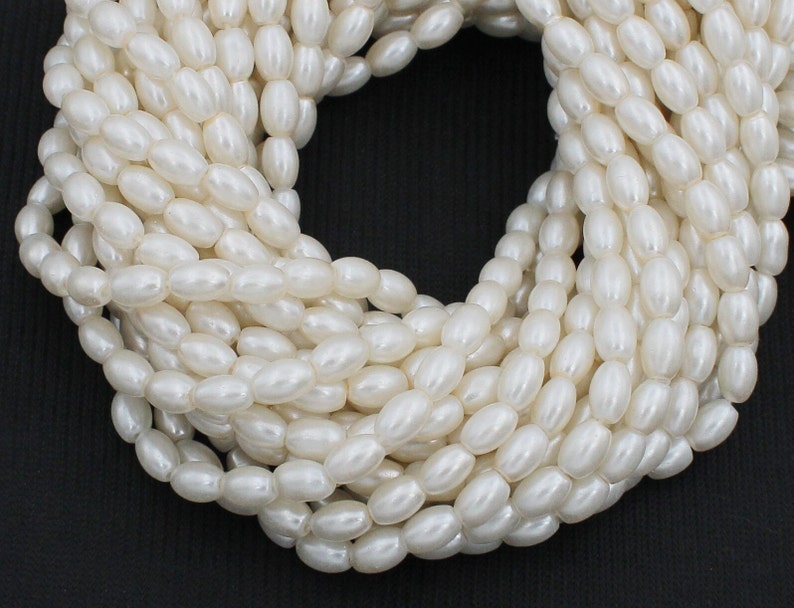 May include: A strand of white oval-shaped beads. The beads are smooth and have a pearlescent finish.