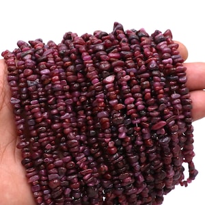 May include: A strand of small, irregular, deep red ruby gemstone beads. The beads are approximately 4mm in size and have a natural, rough texture.