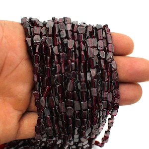 Op de afbeelding: Een streng donkerrode edelsteen kralen, elke kraal heeft een unieke, onregelmatige vorm met een licht gefacetteerd oppervlak. De kralen zijn aan elkaar geregen om een lange ketting of armband te maken.
