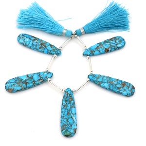 May include: Turquoise gemstone beads with a matrix of brown and silver accents. The beads are strung together with silver-colored metal bars and are topped with two turquoise tassels. The beads are teardrop shaped.