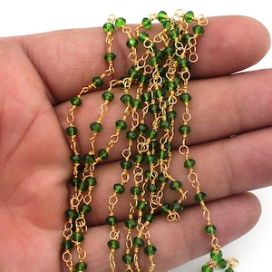 Peut inclure: Gros plan sur un fil de perles vertes facettées enfilées sur un fil doré. Les perles sont d'un vert émeraude profond, et le fil a une finition brillante. Les perles sont petites et espacées uniformément, créant un look délicat. Le bijou est tenu dans une main.