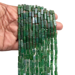 Puede incluir: Hebras de cuentas rectangulares verdes. Las cuentas son de un color verde oscuro, verde bosque, con variaciones de tono. Las cuentas están ensartadas, creando una apariencia fluida y texturizada. El fondo es blanco liso.