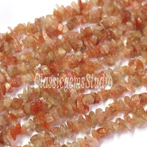 Peut inclure: Un brin de perles en forme de chips de pierre de soleil dans des tons d'orange, rouge et or. Les chips sont de forme irrégulière et ont une apparence translucide.