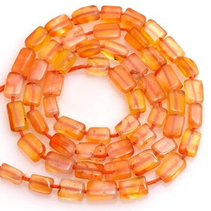 Könnte beinhalten: Eine Kette aus orangefarbenen und gelben rechteckigen Perlen. Die Perlen sind auf einer dünnen, roten Schnur aufgefädelt. Die Perlen haben eine durchscheinende Qualität mit Farb- und Texturvariationen. Der Gesamteffekt ist eine warme, erdige Ästhetik.