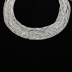 Op de afbeelding: Een streng witte maansteen kralen, ongeveer 4 mm in diameter, gerangschikt in een cirkelvormige patroon op een zwarte achtergrond.