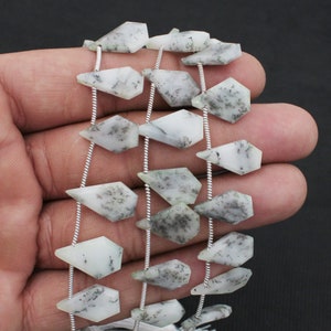 Peut inclure: Un collier de perles en opale dendritique en forme de cerf-volant avec une surface lisse et polie. Chaque perle présente une base blanc laiteux avec des inclusions complexes gris foncé en forme de fougère, enfilées sur un fil d'argent fin.