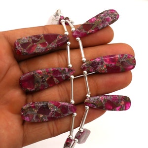 Op de afbeelding: Een streng roze en gouden edelsteen kralen met zilveren tussenstukken. De kralen zijn traanvormig en hebben een gevlekt patroon.