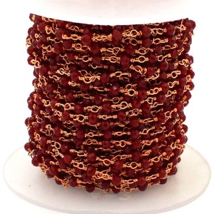 May include: A spool of red gemstone beads strung on a copper chain. The beads are faceted and have a shiny finish. The chain is a delicate, fine gauge.
