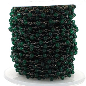 May include: A spool of dark green faceted glass beads strung on a black chain. The chain is made of small, linked metal rings.