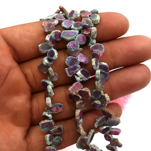 May include: A strand of ruby zoisite gemstone beads, featuring a mix of green, pink, and red hues. The beads are irregular in shape and have a rough, natural finish.