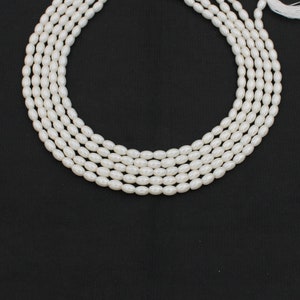 May include: A strand of white oval-shaped pearls, strung together on a white thread. The pearls are arranged in a circle, with the ends of the thread meeting at the top of the circle.