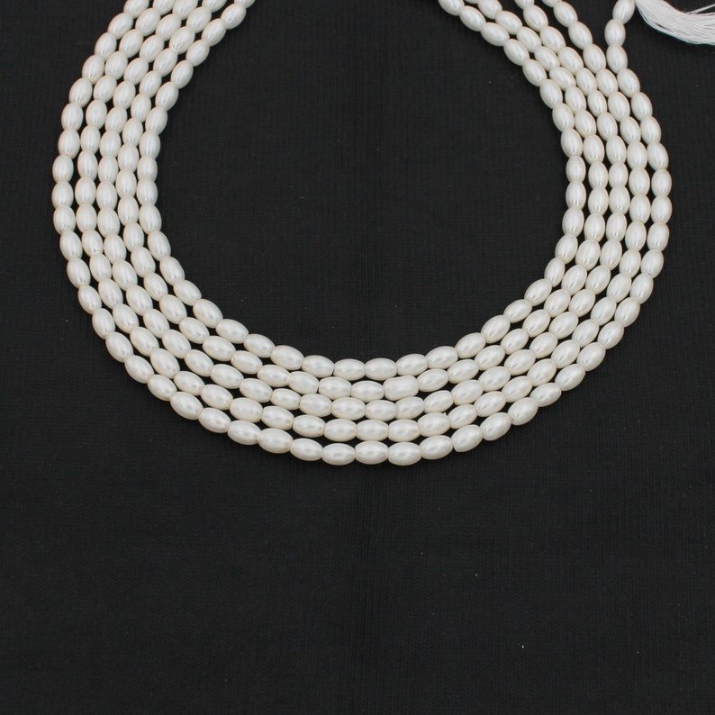 May include: A strand of white oval-shaped pearls, strung together on a white thread. The pearls are arranged in a circle, with the ends of the thread meeting at the top of the circle.
