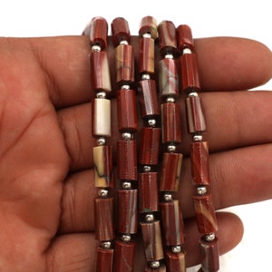 May include: Strands of red and tan gemstone beads with silver-colored spacers. The beads are cylindrical and faceted, creating a textured appearance. The gemstones have natural variations in color and pattern.