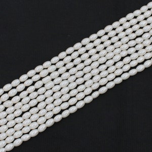 May include: A strand of white oval-shaped pearl beads. The beads are strung together on a clear thread.