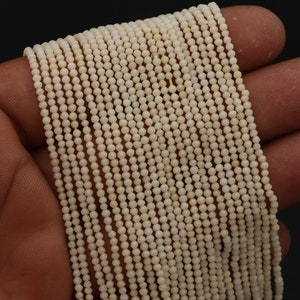 May include: A strand of white faceted gemstone beads. The beads are small and round, and they are strung on a clear thread. The beads are arranged in a straight line, and they are all the same size and shape.