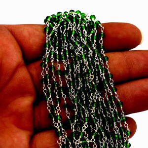 Könnte beinhalten: Eine Strähne grüner Glasperlen, die auf einer silbernen Kette aufgefädelt sind. Die Perlen sind facettiert und haben eine glänzende Oberfläche.
