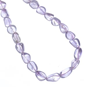 Könnte beinhalten: Eine Halskette mit durchscheinenden, hellvioletten, abgerundeten Edelsteinperlen, die auf einer dünnen, hellvioletten Schnur aufgereiht sind. Die Perlen haben ein glattes, poliertes Aussehen und variieren leicht in Form und Größe. Der Hintergrund ist schlicht weiß.