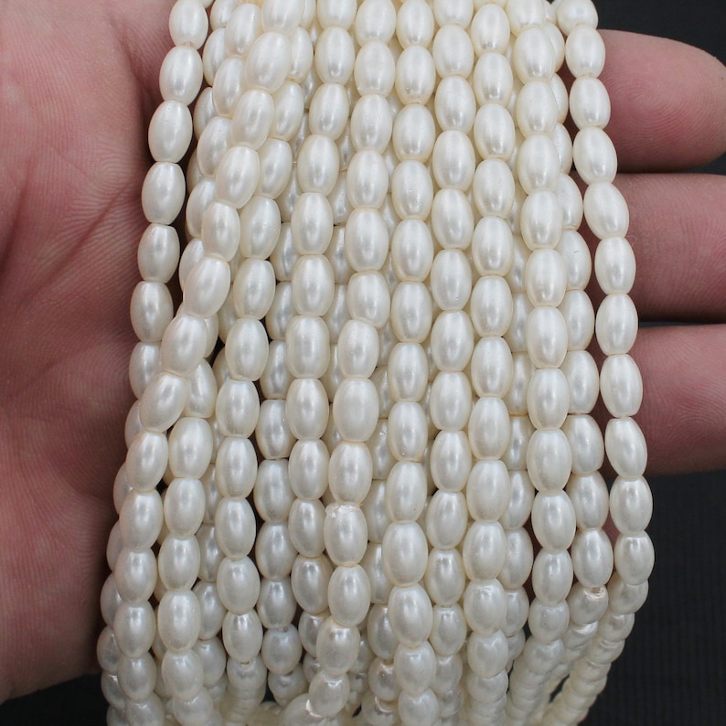May include: A strand of white oval-shaped faux pearl beads. The beads are strung on a clear thread and are approximately 6mm in diameter.