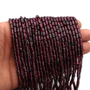 Peut inclure: Gros plan sur des rangées de perles de grenat rouge foncé. Les perles sont rectangulaires et polies. Elles sont enfilées, prêtes pour la création de bijoux. La couleur est un rouge profond et riche.
