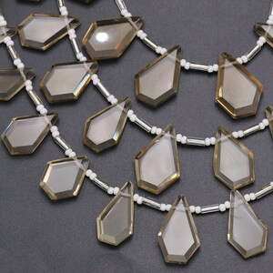 Puede incluir: Un collar hecho con cuentas de cuarzo ahumado facetado en forma de l&aacute;grima y cuentas espaciadoras blancas. El collar est&aacute; hecho con tres hileras de cuentas.