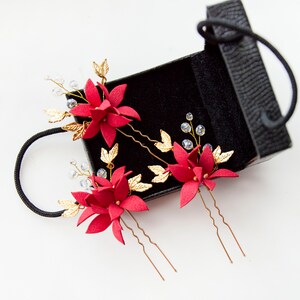 May include: Three red flower hair pins with gold leaves and clear crystals in a black box.