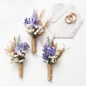 Puede incluir: Tres pequeños ramos de flores moradas y blancas atados con cuerda, con dos alianzas de oro sobre un hexágono de mármol.