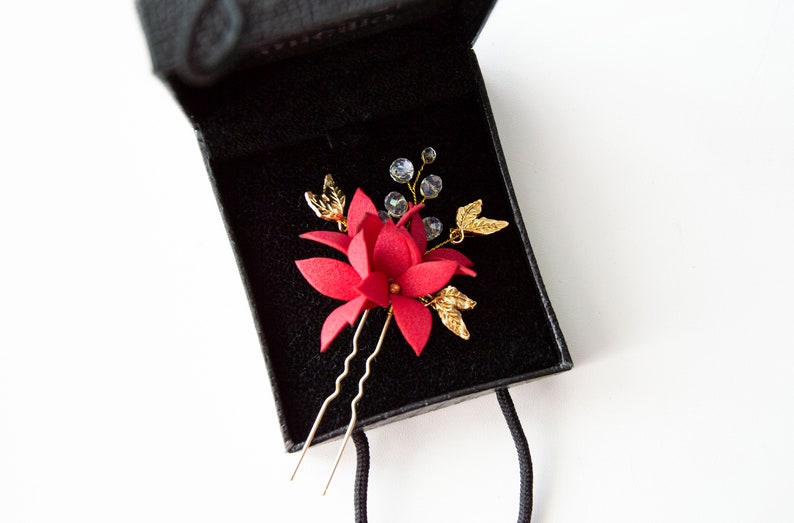May include: A red flower hair clip with gold leaves and clear crystals, in a black velvet box.