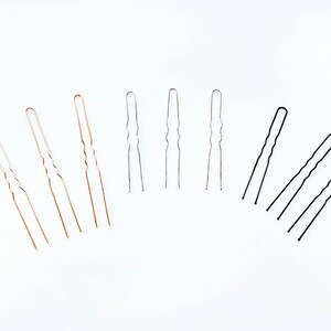 May include: A set of hair pins in three colors: gold, silver, and black. The pins are all the same size and shape, with a wavy design.
