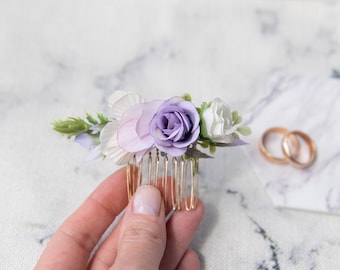 May include: A gold hair comb with a cluster of purple and white fabric flowers. The flowers are arranged in a cascading design.