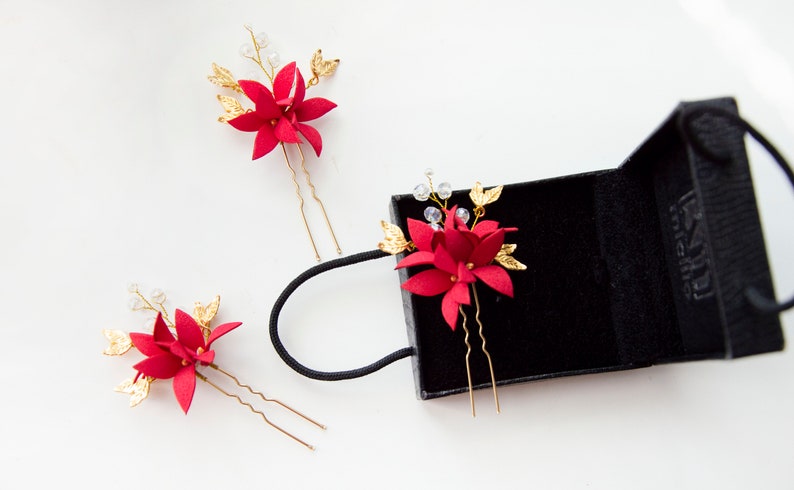 May include: Three red flower hair pins with gold accents and clear beads. The pins are in a black velvet box with a white label that says "K&M Jewelry".