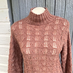May include: A mauve knitted sweater with a high neck and a delicate openwork pattern.