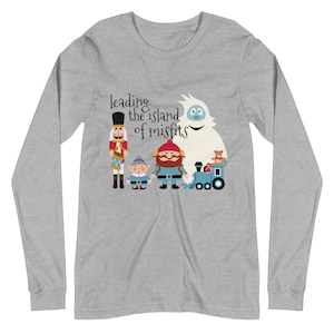 May include: A long-sleeve gray shirt featuring a graphic of characters from the Island of Misfit Toys, including a nutcracker, elf, bearded man, abominable snowman, and a train. The text "leading the island of misfits" is above the characters.