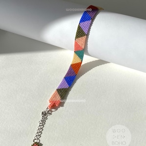 May include: A colourful beaded bracelet with a geometric pattern of triangles in shades of pink, blue, green, and orange. The bracelet has a silver clasp and is made with small, evenly spaced beads.