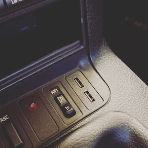 May include: Close-up of a car's dashboard with a black and silver control panel. The panel features a button labeled "HIFI" with a speaker icon, a red light, and two USB ports.