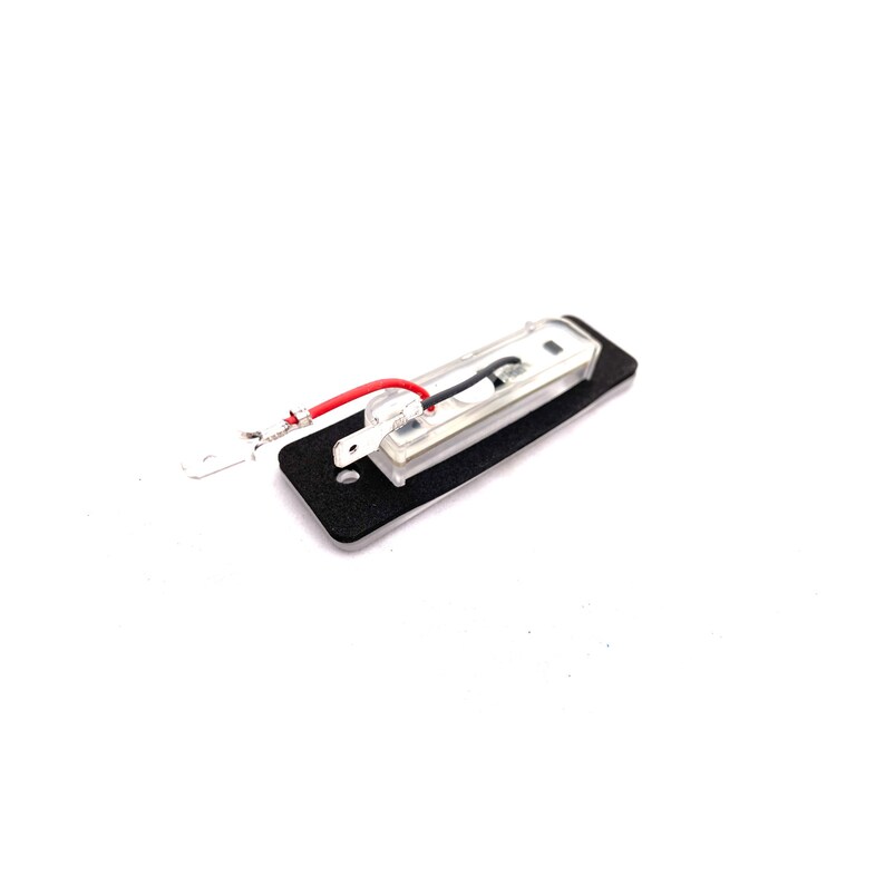May include: A small, clear, rectangular light with black wires and a black backing. The light has two small metal prongs on the side.