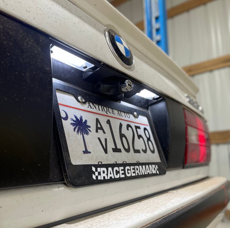 May include: A white car with a black license plate frame. The license plate reads "A16258" and has a palm tree and crescent moon design. The text "Antique Auto" and "Race German" are also on the plate.