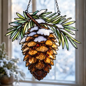 Könnte beinhalten: Glasmalerei-Kiefernzapfen-Ornament, an einer Kette aufgehängt. Der Kiefernzapfen besteht aus bernsteinfarbenem und braunem Glas mit weißen und grünen Akzenten, die Schnee und Tannennadeln imitieren. Eine festliche Dekoration.