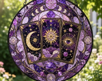 May include: A circular stained glass suncatcher featuring three tarot cards in shades of purple and gold. The center card displays a sun, the left a crescent moon, and the right an eye. The border includes moon phases and stars in a metal frame.