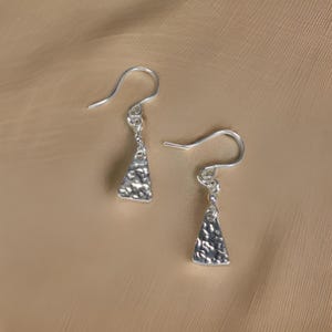 May include: A pair of silver dangle earrings with a textured triangular pendant.