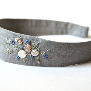 May include: A gray linen headband with embroidered flowers in shades of blue, white, and pink.