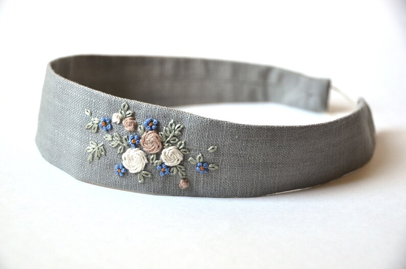 May include: A gray linen headband with embroidered flowers in shades of blue, white, and pink.