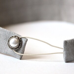 May include: A gray fabric headband with a white pearl button and an elastic band.