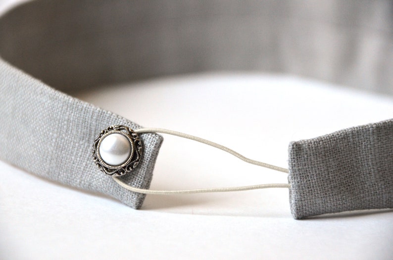 May include: A gray fabric headband with a white pearl button and an elastic band.