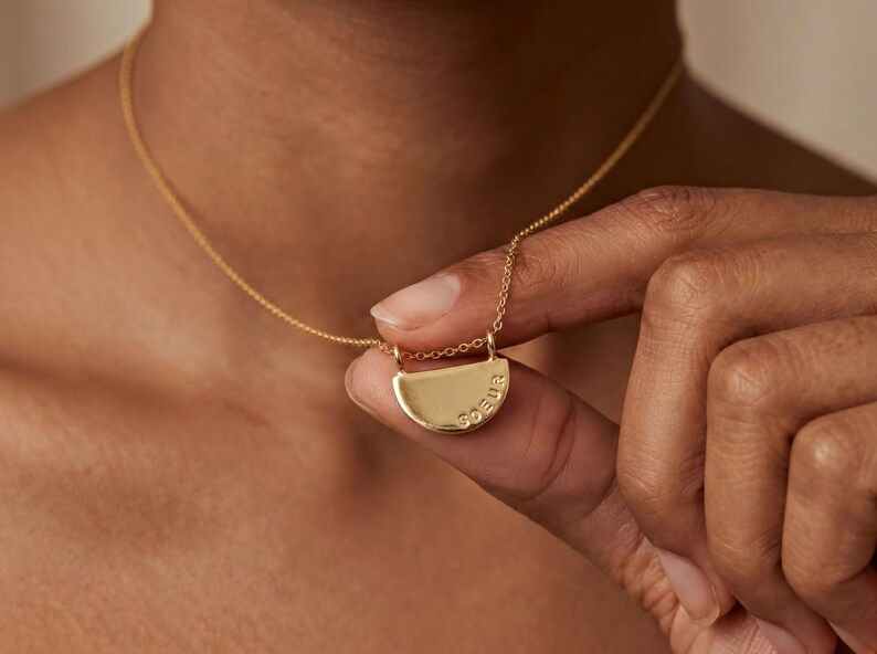 A close-up of a person's hand holding a gold necklace with a pendant.