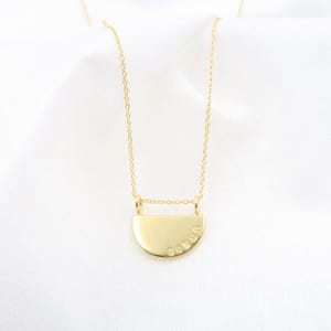 A gold-colored necklace with a pendant in the shape of a circle, featuring the word "SELU" engraved on it.