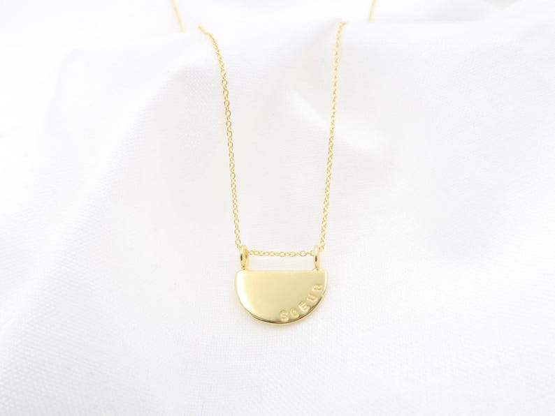A gold-colored necklace with a pendant in the shape of a circle, featuring the word "SELU" engraved on it.