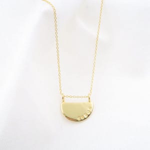 A gold-colored necklace with a pendant in the shape of a circle, possibly a charm or a symbol.