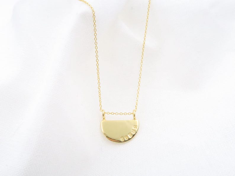 A gold-colored necklace with a pendant in the shape of a circle, possibly a charm or a symbol.