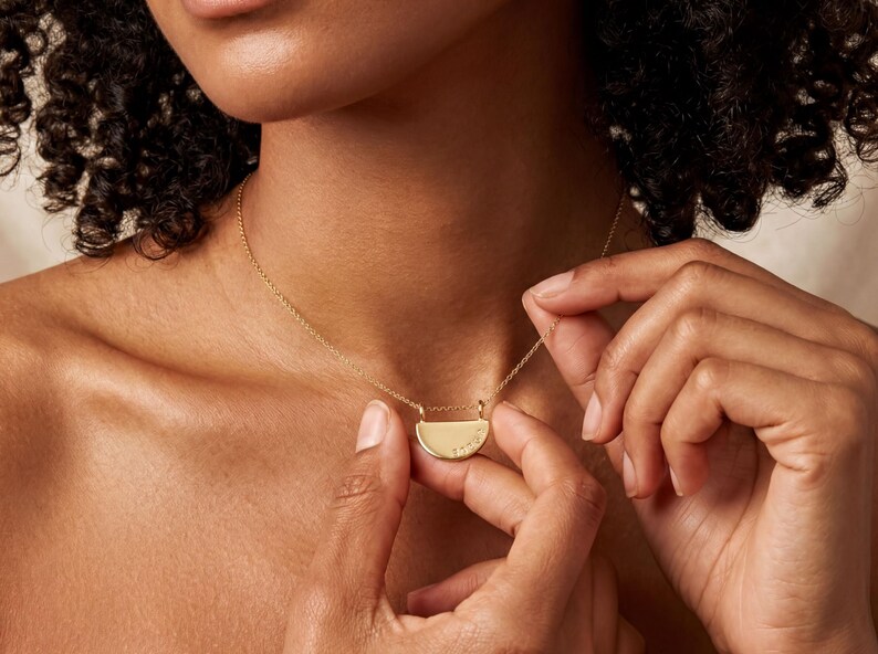 A close-up of a person's neck and chest wearing a gold necklace with a pendant.