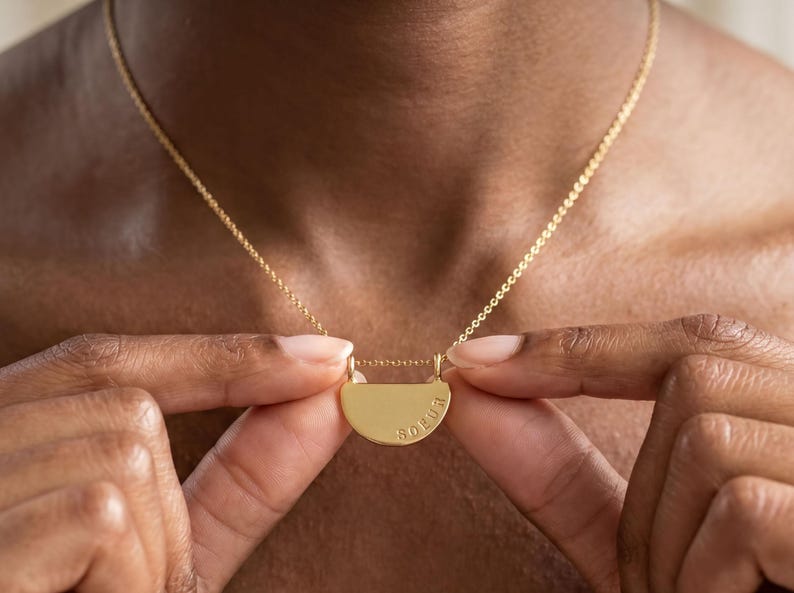 A close-up of a person's hands holding a gold necklace with a pendant.